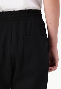 Black cotton sweatpants featuring an elastic waistband and a patch pocket on the back, with a smooth texture and minimalist design.
