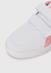 White children's sneaker with two velcro straps and pink polka dot detail near the heel on a white background.
