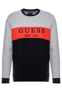 Sudadera de cuello redondo con bloques de color que presenta paneles en gris, rojo y negro, con "GUESS EST. 1981" bordado en negro. Fabricada en tejido suave.