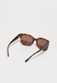 Ochelari de soare de țestoasă cu lentile maronii, design cu cadru pătratit și accente aurii pe tâmple. Finisaj neted cu textură lucioasă.