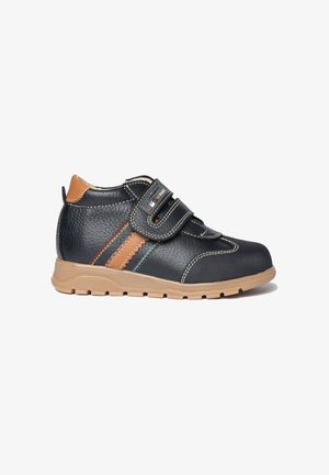 Zapatilla deportiva para niños negros con suela color canela, dos tiras de velcro, rayas laterales en tonos canela y multicolor, y puntera reforzada.