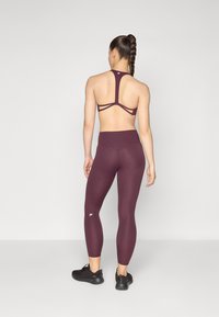 Set atletico bordeaux composto da un top corto con spalline e leggings a vita alta con una texture liscia. Sneakers nere completano il look.