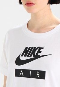 Weißes Baumwoll-T-Shirt mit einem großen schwarzen Nike-Logo und "AIR"-Text darunter, runder Ausschnitt und kurze Ärmel, glattes Stoffgefühl.