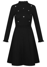 Robe noire à manches longues avec haut côtelé, col et poignets volantés, jupe évasée, et petits ornements décoratifs en forme d'abeille en cristal sur la poitrine.