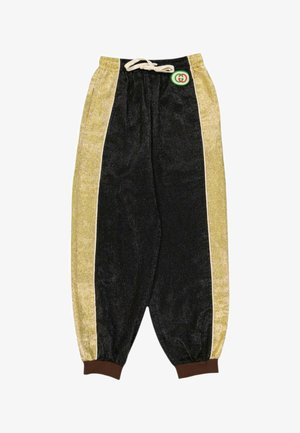 Pantalon en velours noir et or avec des poignets élastiques, une taille à cordon crème et un petit logo rond vert et rouge près de la ceinture.