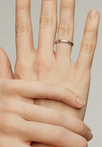 Anillo de plata con una banda texturizada llevado en un dedo, manos superpuestas con tono de piel natural y características visibles de los dedos.
