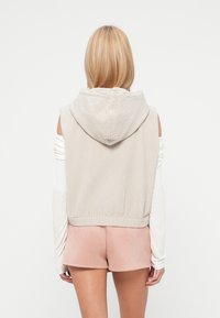 Ανοιχτό γκρι cropped φούτερ με μεγάλο κουκούλα, ριμπ υφή και ελαστική πλέξη στη μέση, συνδυασμένο με απαλό ροζ σορτς. Διακριτική σχεδίαση ανοιχτού ώμου.