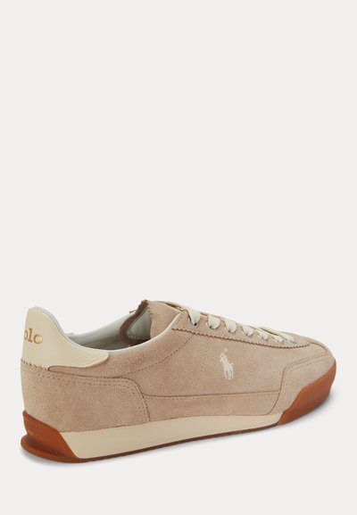 Baskets basses en daim beige avec lacets blancs, semelle en caoutchouc marron et petit logo blanc de joueur de polo sur le côté.