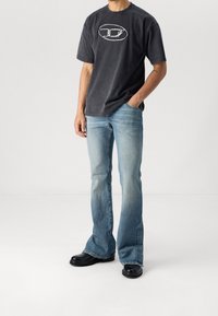 Camiseta negra de manga corta con estampado gráfico, combinada con jeans de campana azul claro y calzado negro, exhibida sobre un fondo neutro.