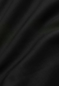 Tela negra lisa con pliegues diagonales sutiles y una textura fina visible bajo una luz suave.