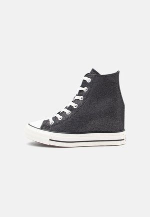 Zwarte hoge canvas sneaker met witte rubberen zool, witte neuskap en witte veters, zij-aanzicht op een effen achtergrond.