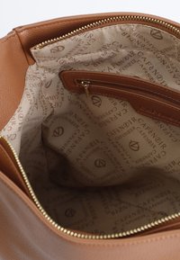 Interno di una borsa in pelle marrone con una texture liscia, dotato di una tasca con zip e foderato con un motivo beige con logo ripetuto.