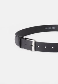 Čierny kožený opasok s kovovou sponou v striebornom odtieni, hladkým povrchom a viacerými dierkami na prispôsobenie. Klasický dizajn, vhodný na rôzne outfity.