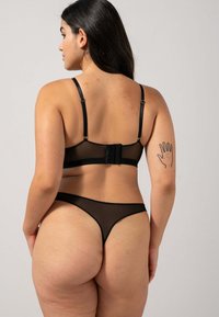 Ensemble de lingerie noire en voile comprenant un bralette avec des bretelles ajustables et une fermeture à crochets, accompagné d'un thong assorti. Texture lisse.