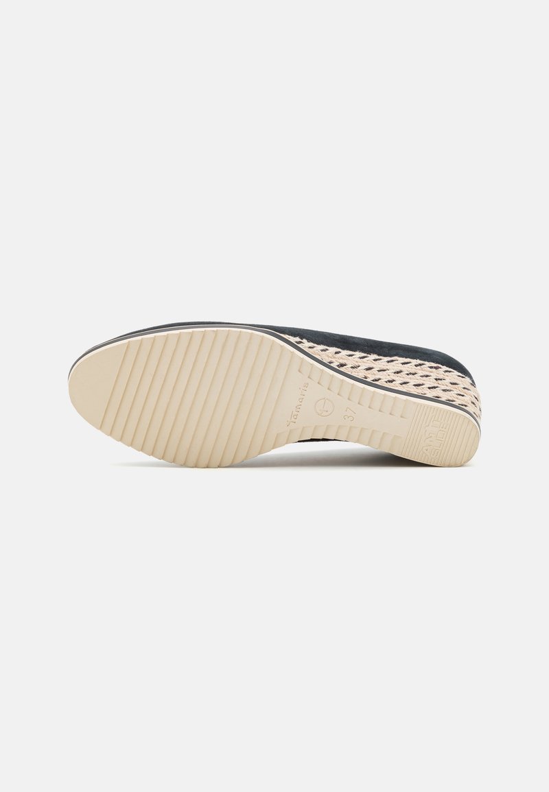 Zwarte suède schoen met geweven beige accenten, rubberen zool met verticale groeven, en tan onderlabels. Plat ontwerp voor gemakkelijk dragen.