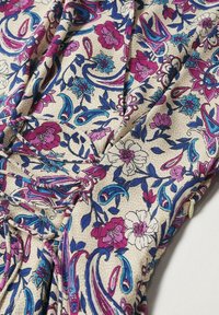 Tissu à motif floral présentant des fleurs roses, bleues et blanches sur un fond beige. Surface texturée avec un design drapé et des plis subtils.