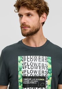Donkergrijze katoenen t-shirt met een levendige groene grafische print met tekst en een patroon van ronde vormen. Korte mouwen, ronde hals.