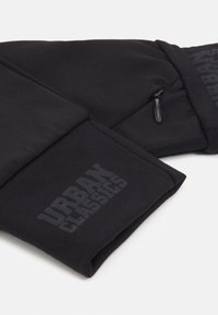 Pantaloni de jogging negri, realizati dintr-un material textil fin, avand un logo proeminent "URBAN CLASSICS" cu finisaj mat si o mică buzunar cu fermoar.