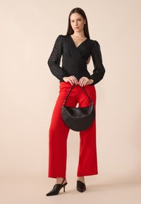 Haut noir à manches texturées, pantalon rouge à jambes larges et un sac à main noir rond avec une sangle tressée, associé à des mules à talons noirs.