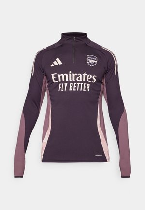 Maglia sportiva a maniche lunghe di colore viola scuro con pannelli laterali a contrasto di rosa chiaro. Presenta colletto con mezza zip e logo "Emirates Fly Better".