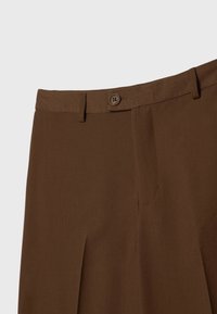 Pantalon plissé marron avec fermeture par bouton et fermeture éclair, doté de passants de ceinture le long de la taille.