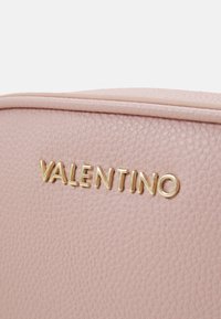Rosa skinnveske med teksturert overflate og gull "VALENTINO"-logo. Glatte, rundede kanter og minimalistisk design er synlig.