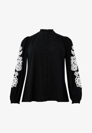Blouse noire à manches bouffantes longues, avec des motifs floraux brodés en blanc sur les manches. Boutons à l'avant et col froncé.