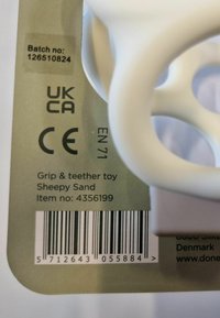 Valge käepide ja närimismänguasi ümmarguse disainiga. Toote üksikasjad ja puhverkood rohelisel taustal. Nähtavad CE ja UKCA märgised.