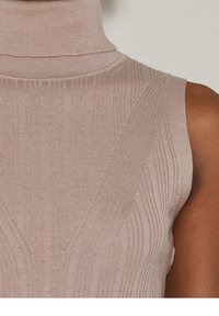 Ärmförsedd tunika i ljusbeige stickad tyg; har vertikal ribbning och diagonala stickade mönster på framsidan och kragen.