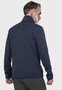 Marineblaue Fleecejacke mit hohem Kragen, strukturiertem Stoff und Seitennähten. Verfügt über einen kleinen grünen Akzent am Kragen.