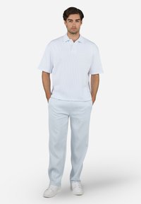 Polo shirt bianco a maniche corte con motivo testurizzato, abbinato a pantaloni leggeri blu chiaro con pince e sneaker bianche.