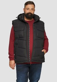Schwarze Steppweste mit Kapuze, zwei Fronttaschen, einem Reißverschluss mit Textakzent und einer lässigen Passform über einem roten Pullover.