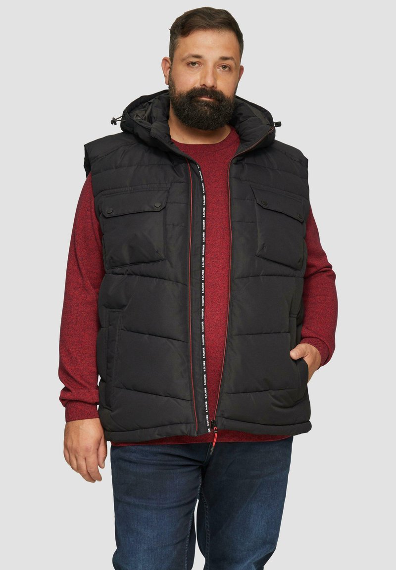 Schwarze Steppweste mit Kapuze, zwei Fronttaschen, einem Reißverschluss mit Textakzent und einer lässigen Passform über einem roten Pullover.