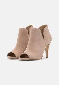 Stivaletti beige in suede con punta aperta e alto tacco a stiletto, caratterizzati da un design con ritagli e texture liscia.