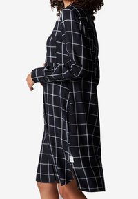 Svart och vit rutad klänning med långa ärmar, sidofickor och en ficka på bröstet. Mjuk tyg med en avslappnad passform.
