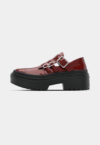 Scarpe con platform in pelle verniciata rossa e suole in gomma nera, caratterizzate da due cinturini regolabili in metallo argentato che attraversano il collo del piede.