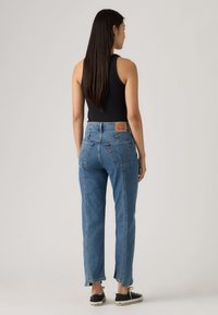 Μπλε τζιν ψηλόμεσο, κατασκευασμένο από denim με ελαφρώς φαρδιά εφαρμογή, διαθέτοντας πίσω τσέπες και ένα δερμάτινο λογότυπο στη ζώνη της μέσης.