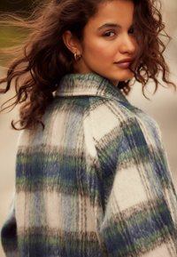 Cappotto a quadro in lana bianco, blu e verde. Presenta grandi motivi a quadri, un collo e un finish morbido e testurizzato.