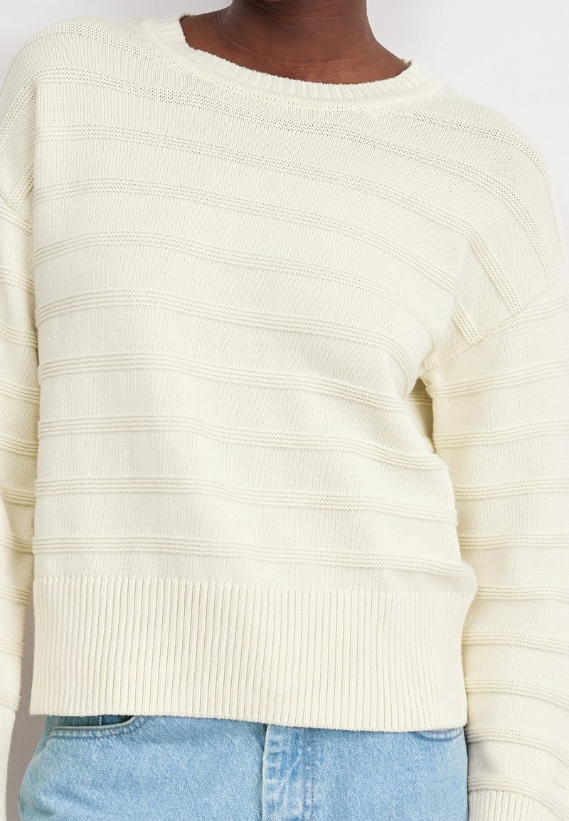 Maglione a maglia color crema con righe orizzontali, polsini e orlo a coste, caratterizzato da un collo rotondo e un tessuto testurizzato.
