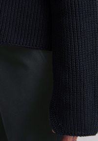 Navy knitted sweater fabric with a ribbed texture. The sleeve has a thick, cuffed design, showing detail and craftsmanship.