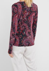 Long-sleeve shirt featuring a paisley pattern in red, pink, and blue on a dark background. Rounded neckline and fitted sleeves.