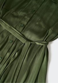 Robe en satin vert olive avec un devant boutonné, deux poches poitrine et une ceinture assortie à la taille pour un ajustement personnalisé. Texture lisse.