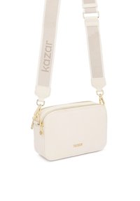 Väike ristkülikukujuline kreemikas õlakott kuldsete tõmblukkude ja metalldetailidega, reguleeritava laiusega kangast rihmaga, millel on "kazar" kirjaga bränd.