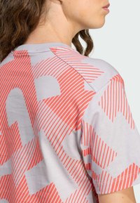 Jasnoszara koszulka z wyrazistym koralowym wzorem graficznym z ukośnymi paskami, krótkimi rękawami i okrągłym dekoltem. Miękka tekstura tkaniny.