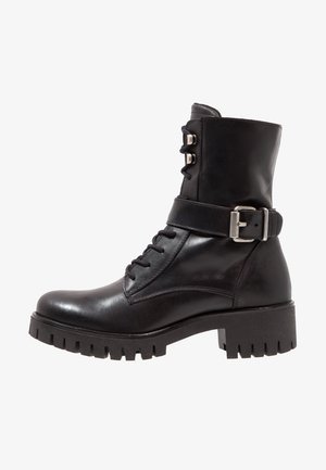 Black leather ankle boot with a lace-up front, adjustable metal buckle, and chunky tread sole. Features a smooth finish and structured design.