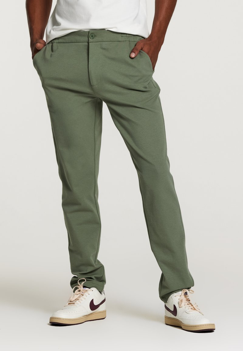 Pantaloni din bumbac verde cu un croi lejer, dotati cu buzunare laterale si inchidere cu nasture. Asociati cu adidași albi și vișinii.