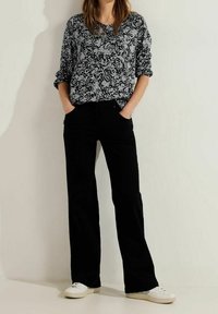 Black wide-leg pants paired with a loose-fitting gray and black patterned long-sleeve top. White sneakers complete the outfit.