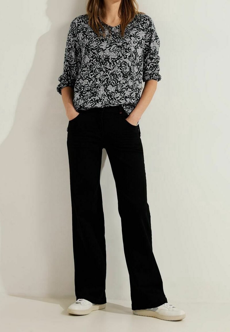 Black wide-leg pants paired with a loose-fitting gray and black patterned long-sleeve top. White sneakers complete the outfit.