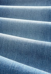 Țesătură de denim bleu deschis cu țesătură twill vizibilă și textură subtilă, afișând pliseuri pliate și o suprafață moale și netedă.