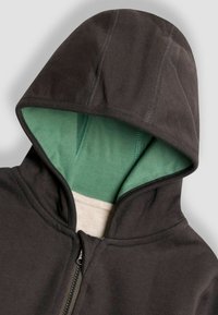Felpa con zip di colore grigio scuro, con fodera interna verde e tessuto testurizzato. Dispone di un cappuccio, cuciture visibili e una zip frontale.